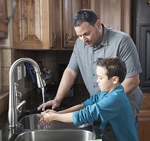 Un hombre ayuda a un niño a lavarse las manos en el fregadero de la cocina.