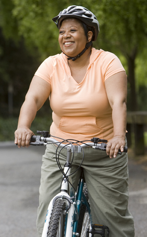 Mujer con sobrepeso que anda en bicicleta por una calle de campo.