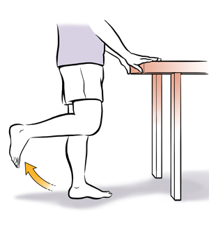 Person from waist down with hands on a table bending on leg up at the knee. 