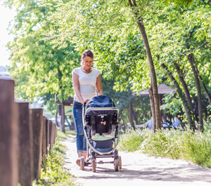 Woman walking outdoors with baby in a stroller.